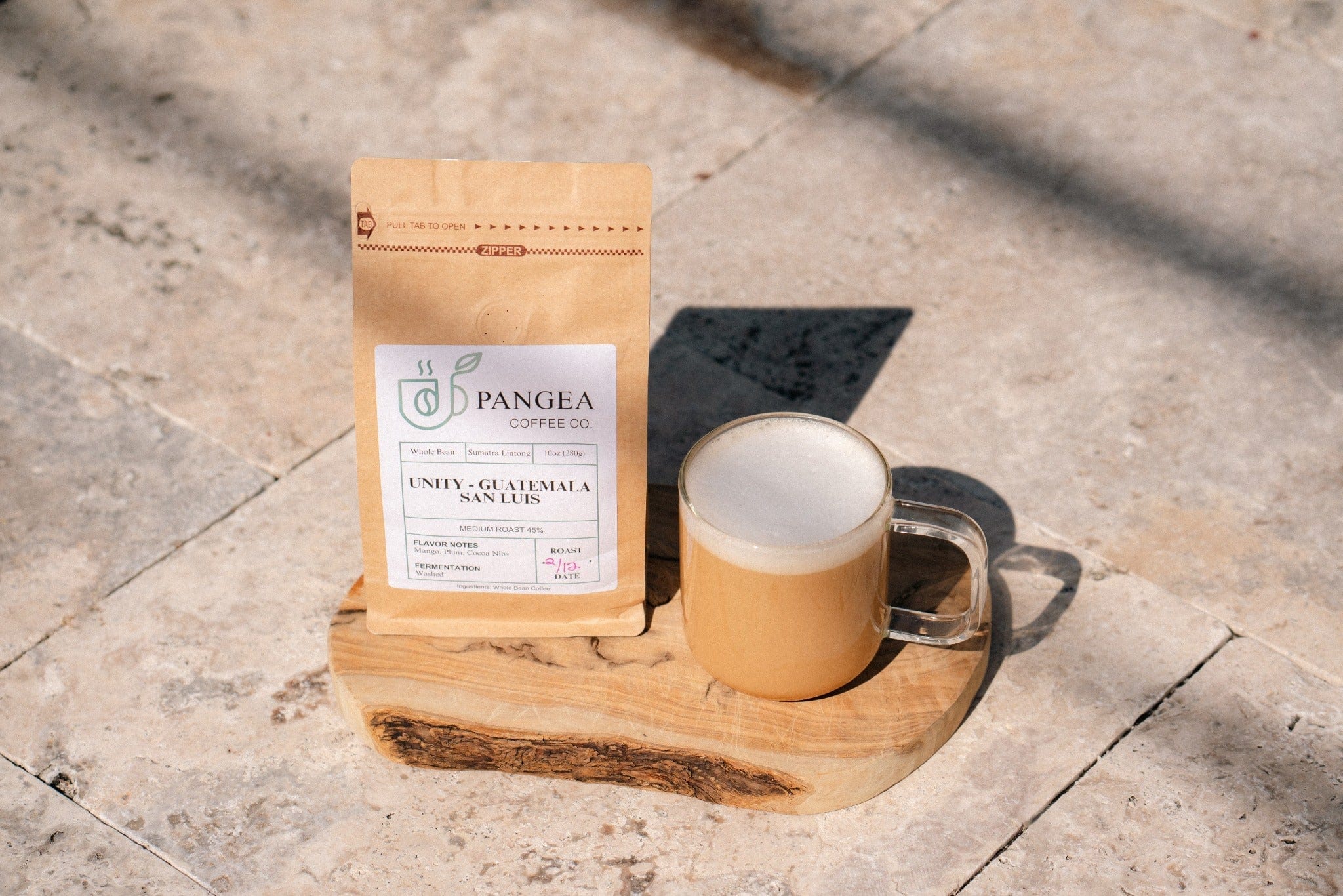 Pangea Coffee bag with a creamy latte on a live-edge wood board in warm sunlight — low acid, allergen-free