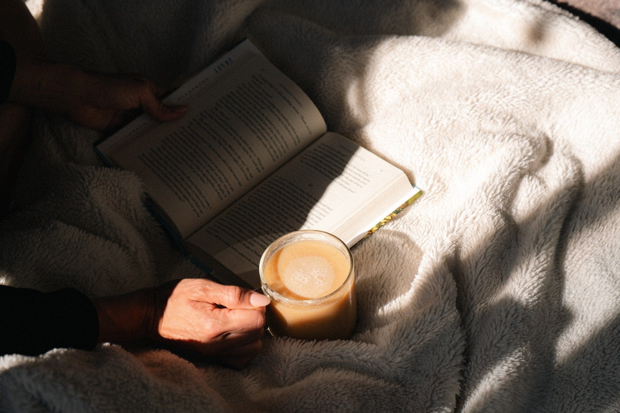 Person relaxing with a book and a warm cup of Pangea Coffee — low acid, gentle on the stomach