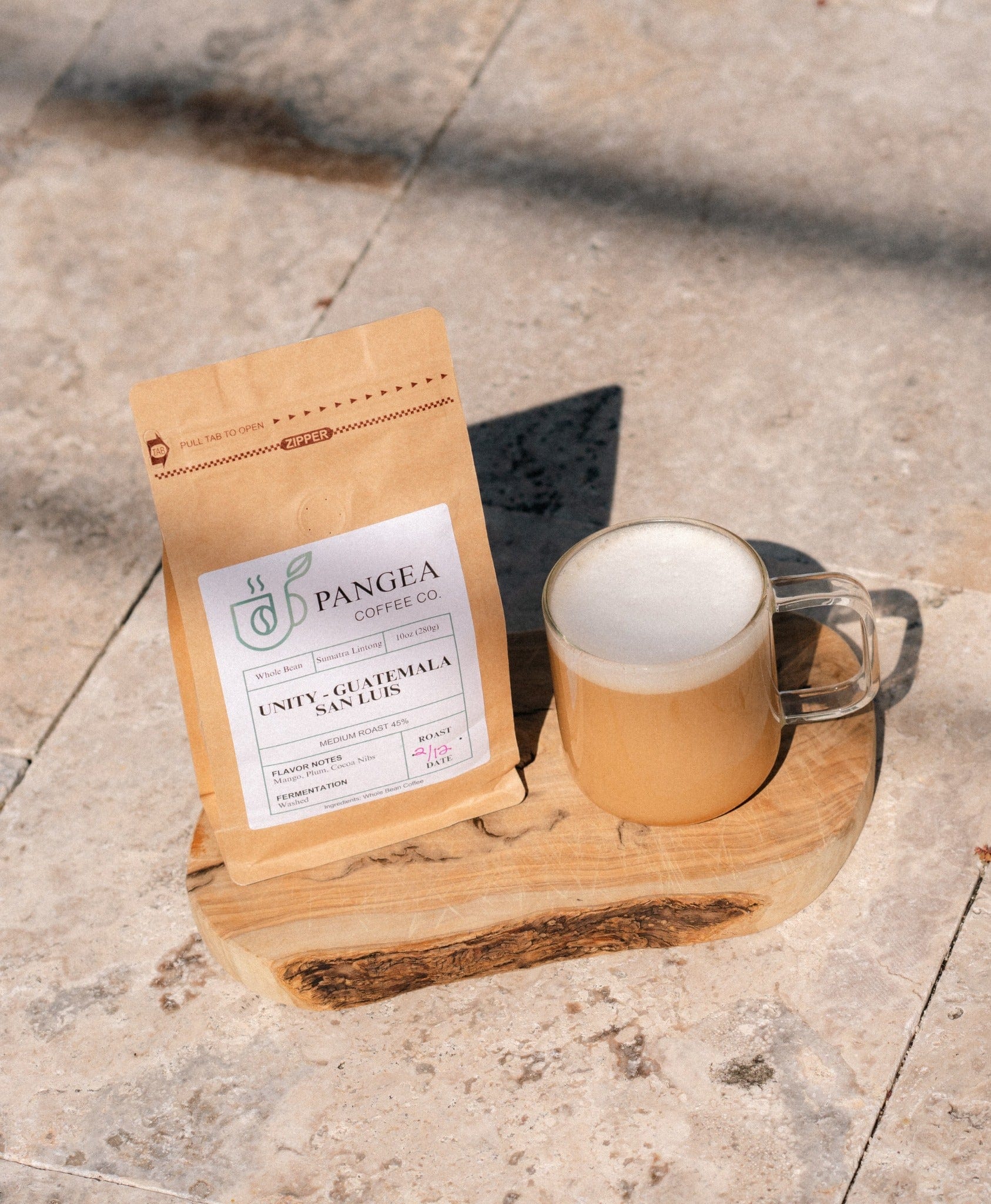 Creamy latte beside a Pangea Coffee bag on a rustic wood board outdoors — low acid, mold-free, gentle coffee