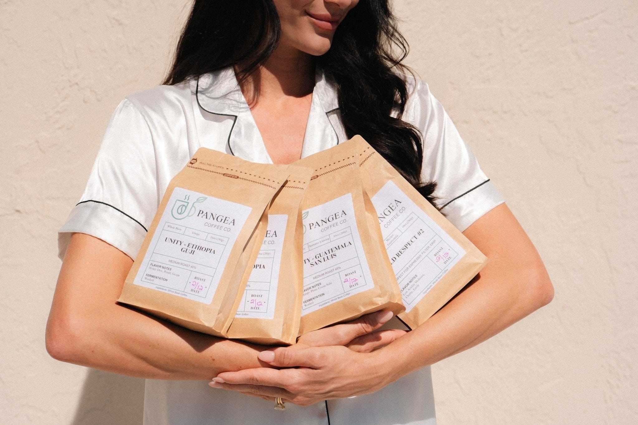 Smiling woman holding four different bags of Pangea Coffee – showcasing variety, happiness, and love for clean, specialty-grade coffee.